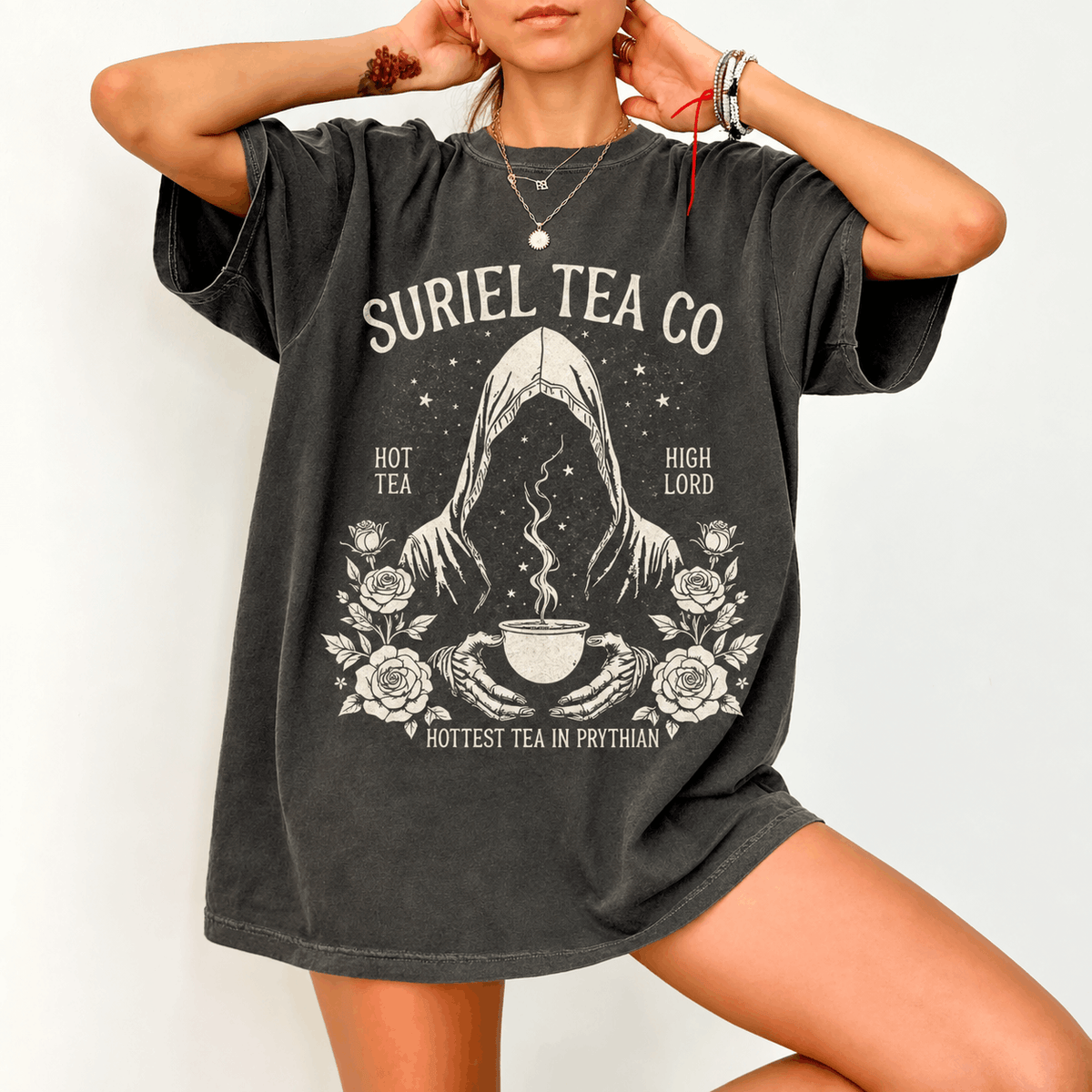 Bookish Closet Suriel Tea Co T-shirt with a hooded figure holding a steaming cup, roses, stars and cream lettering on a dark garment
